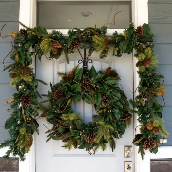 A mangnolia garland across the top of a door with a matching wreath hanging from the door.