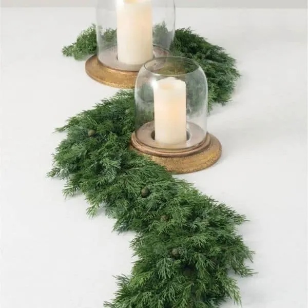 A cedar garland laying curved on a table with candles.
