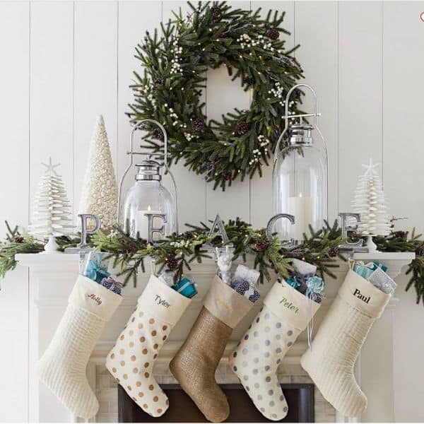 A garland on a white mantel with white stockings and white christmas trees and the word PEACE.