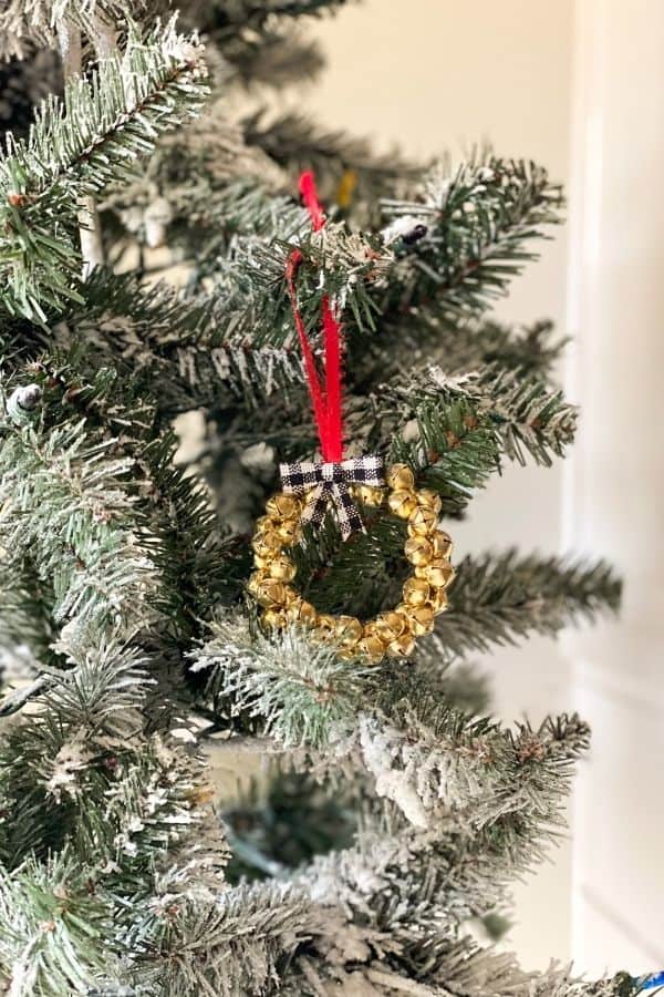 The jingle bell ornament hanging from a flocked Christmas tree.