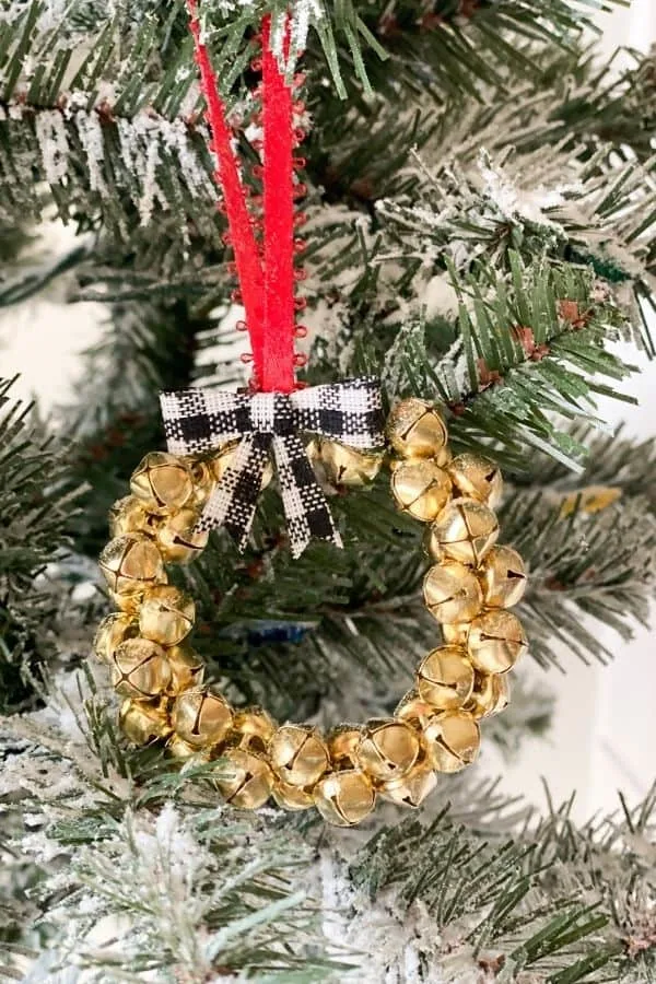 A jingle bell ornament with black and white bow and red ribbon hanging on a Christmas tree.