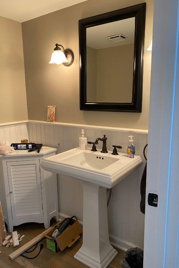 White wainscoting, white pedestal sink, gray walls and a mess of tools all over the floor.