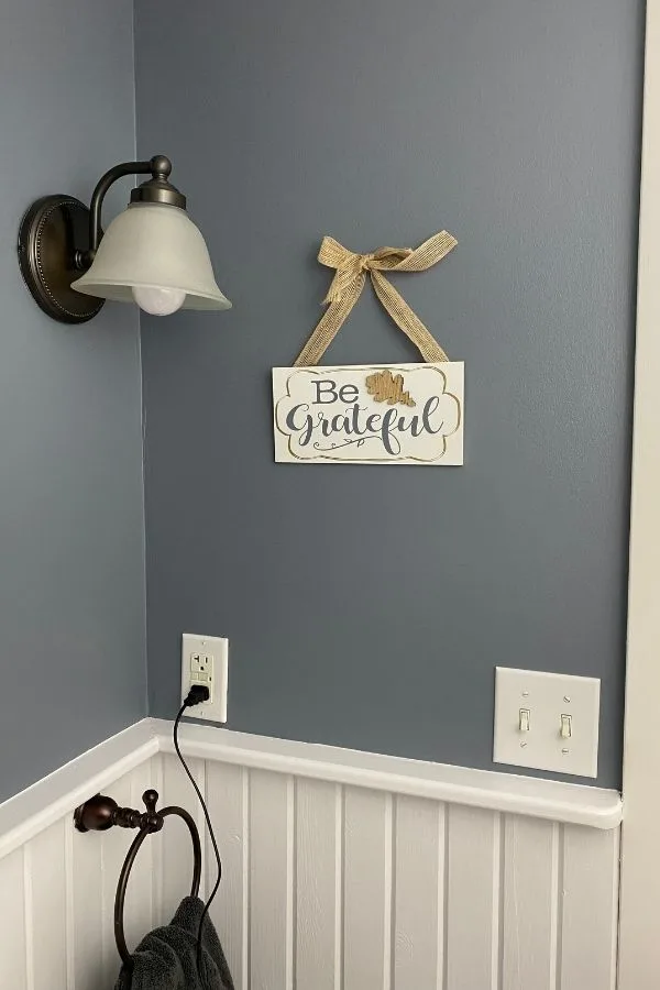 White wainscoting, blue gray walls and a be grateful sign hanging on the walls.