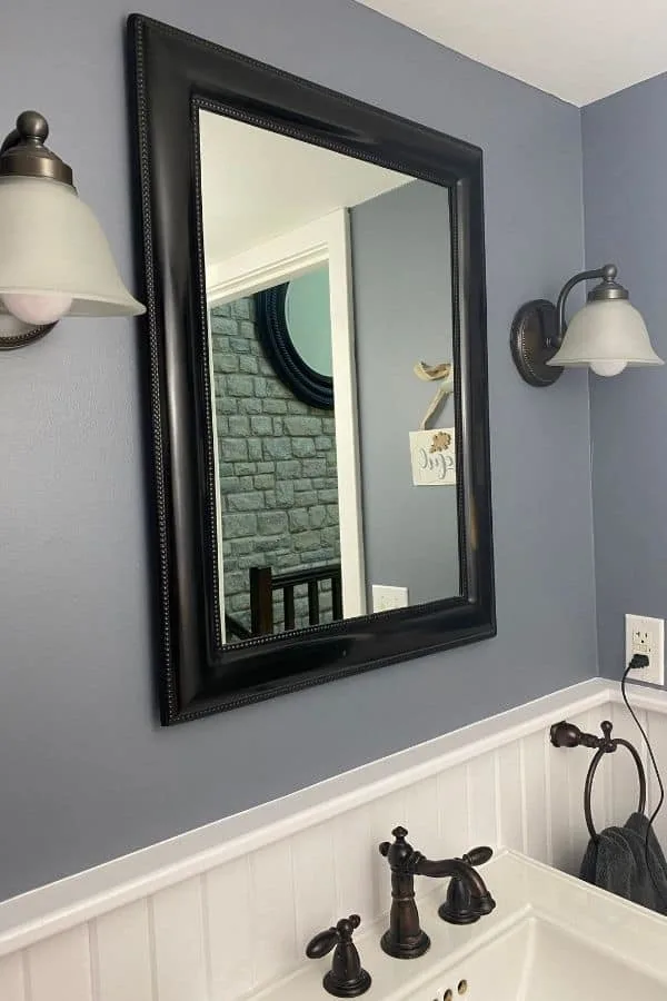 A mirror and two wall sconces in oil rubbed bronze and blue gray walls.