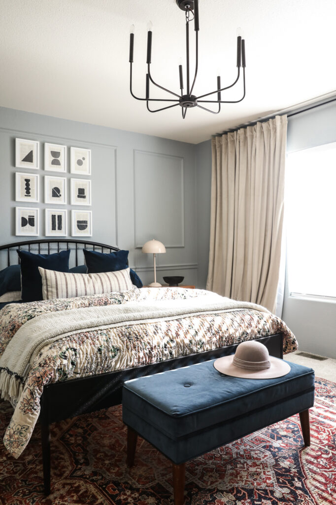 A bedroom with Boothbay Gray on the walls, beige curtains, a black chandelier and a black iron bed.
