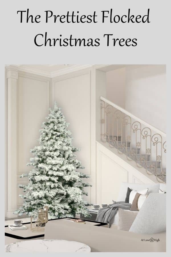 a family room with a flocked Christmas tree in a corner and a stairwell with beige wrought iron.