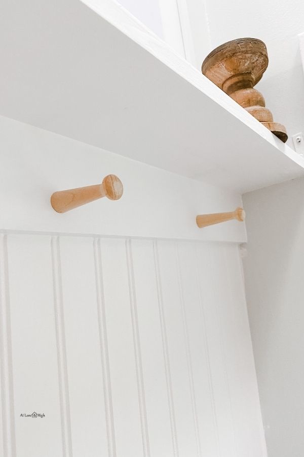 Pegs on the board above beadboard that are raw wood while everything else is white.