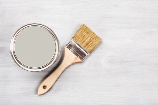 The view of the top of a paint can and a paintbrush laying next to it.