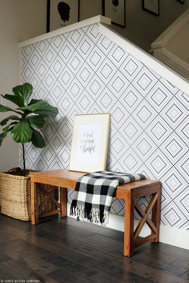 The outside of a staircase wall with wallpaper in a geometric pattern, a wood console table and a fiddle leaf fig next to it.