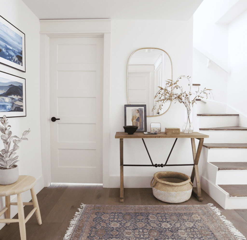 A hallway and stairwell with a desk, basket under the desk and a gold oval mirror above.