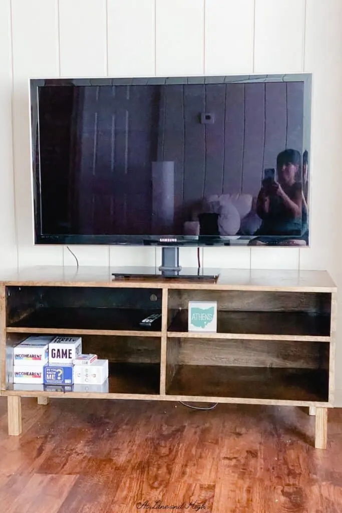 The finished TV stand with a tv on it, some games and an Athens decor sign.