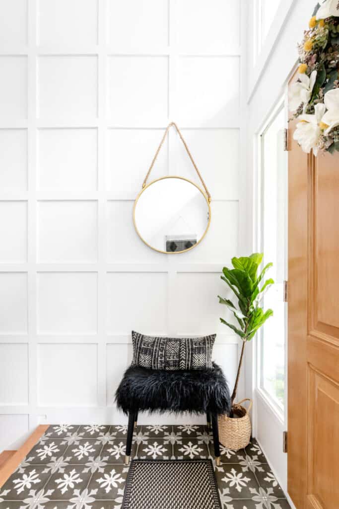 an entryway wall with board and batten, a round mirror hanging and a stool under the mirror with black fur on it.