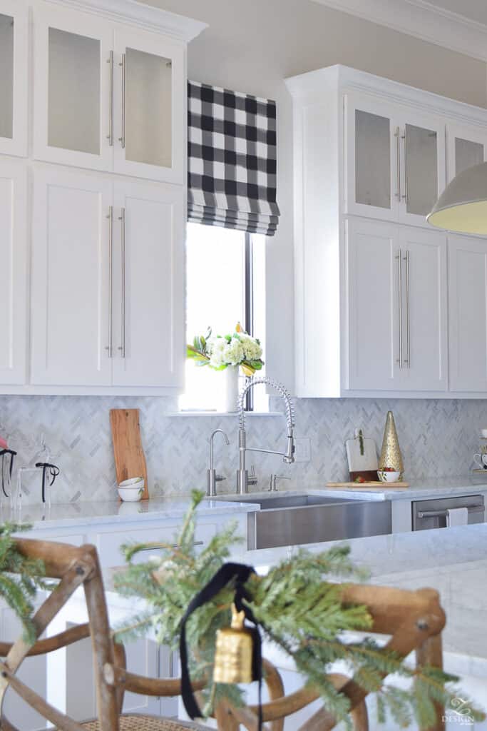 Decorators White by Benjamin Moore is used on cabinetry with a marble herringbone backsplash, black and white buffalo check roman shade and silver hardware.