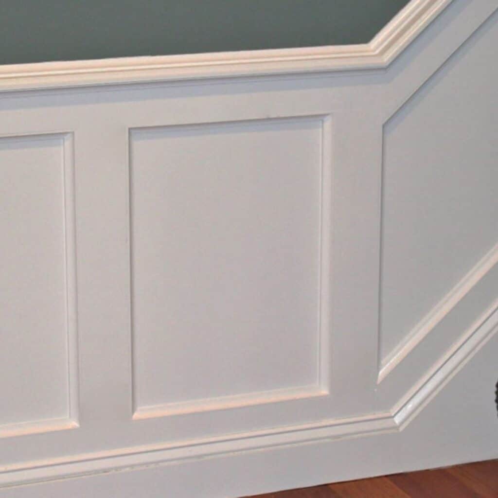 Flat panel wainscoting painted white with a dark green wall above.