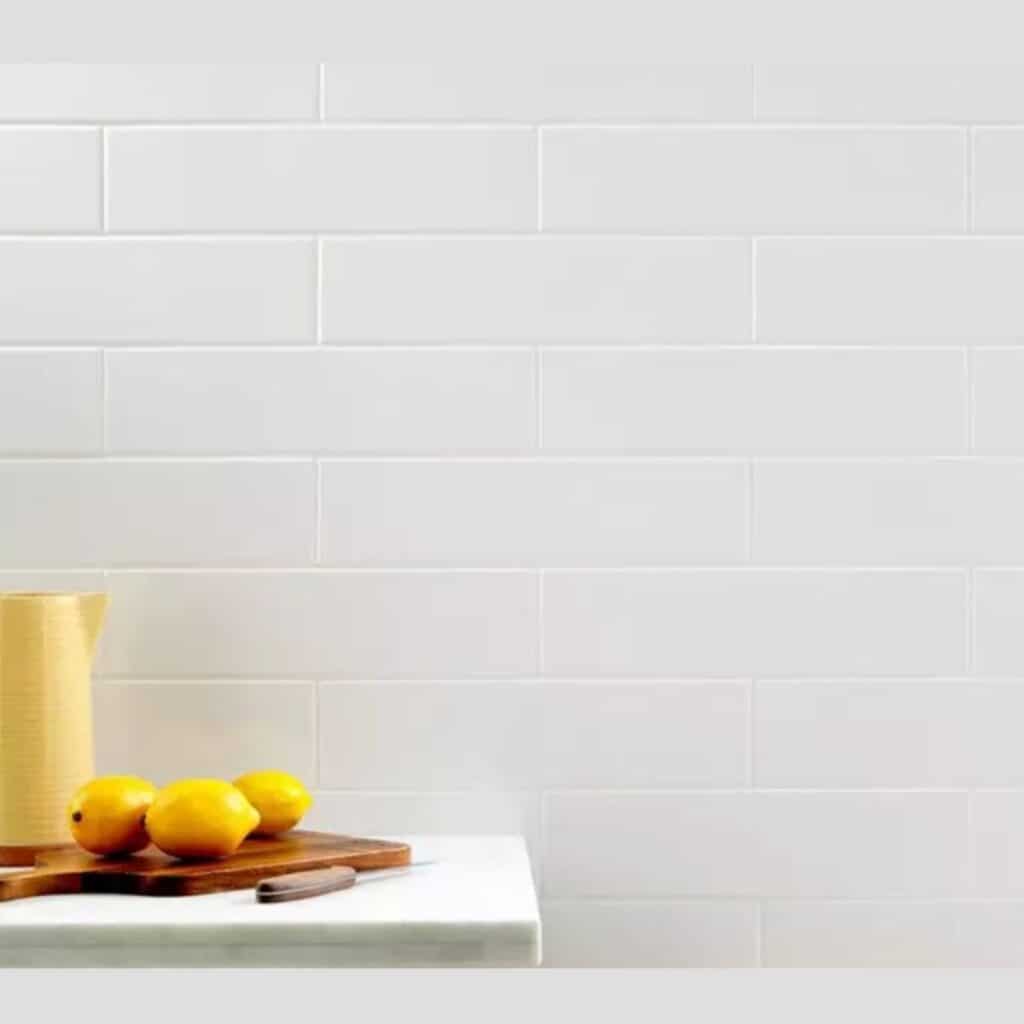 White subway tile with white grout, a yellow pitcher with a cutting board and lemons.