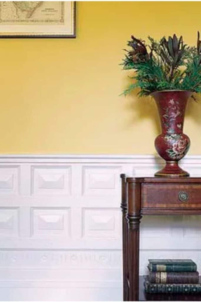 Overlay wainscoting with yellow walls above a wood table with a vase on it.