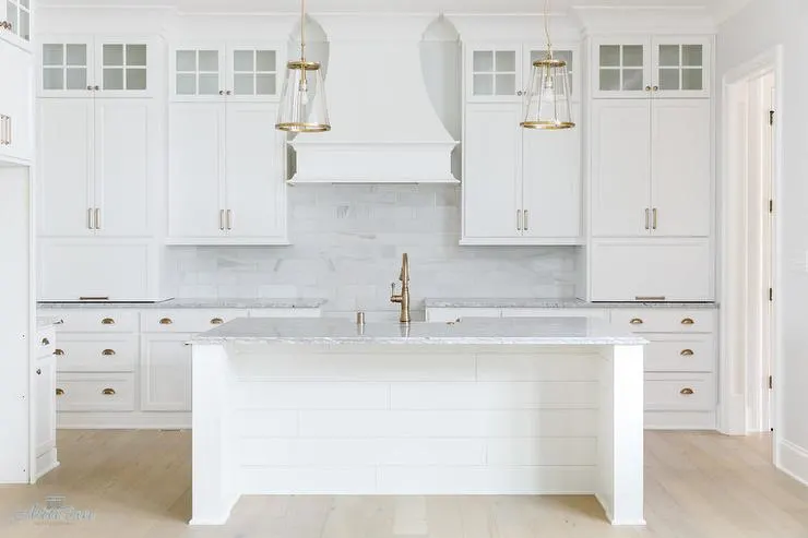 This kitchen has white cabinets in Sherwin Williams Pure white, gold hard ware and a marble subway tile backsplash.