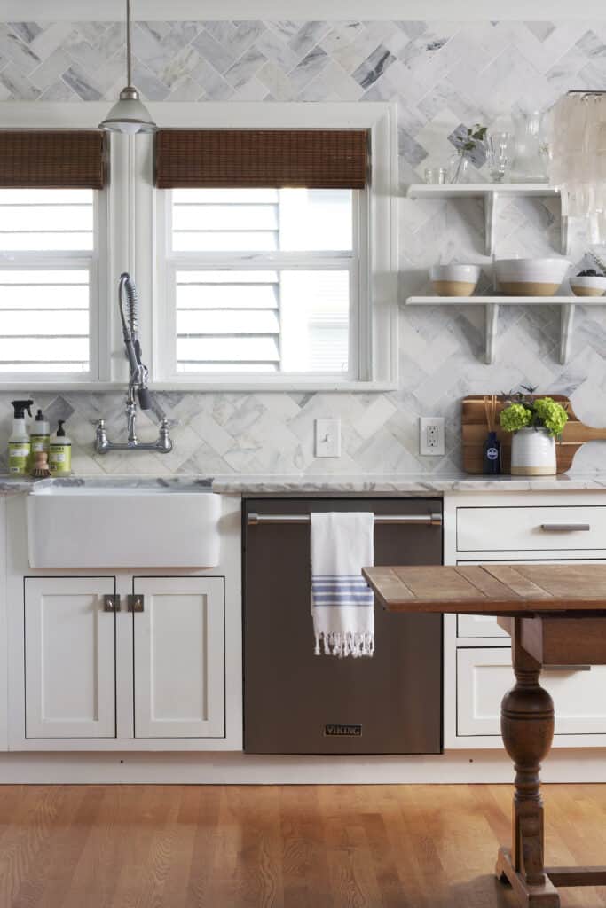 This kitchen has cabinets pained in Benjamin Moore Simply White wiht a marble subway tile backsplash in a herringbone pattern.