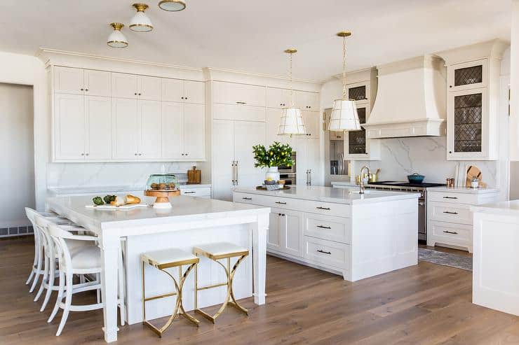 This kitchen has two islands painted Snowbound by Sherwin Williams with gold hardware and light fixtures and quartz counters that look like marble.