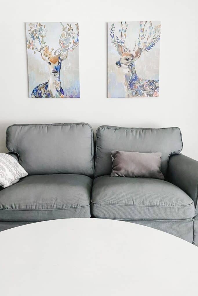 This is my IKEA Uppland sofa, a dark gray lumbar pillow and two pieces of artwork hanging above the couch of deer with flowers in thier antlers.