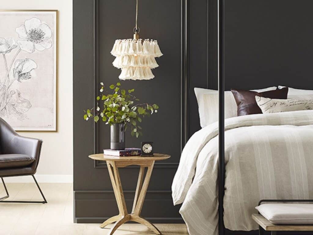 Urbane bronze used on walls in a bedroom with a bed that has light neutral bedding, a hanging light with fringe and a light wood toned end table.