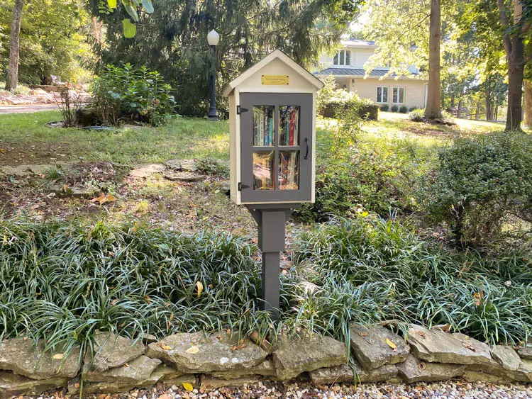 A small bird house looking library in the front yard of a home.