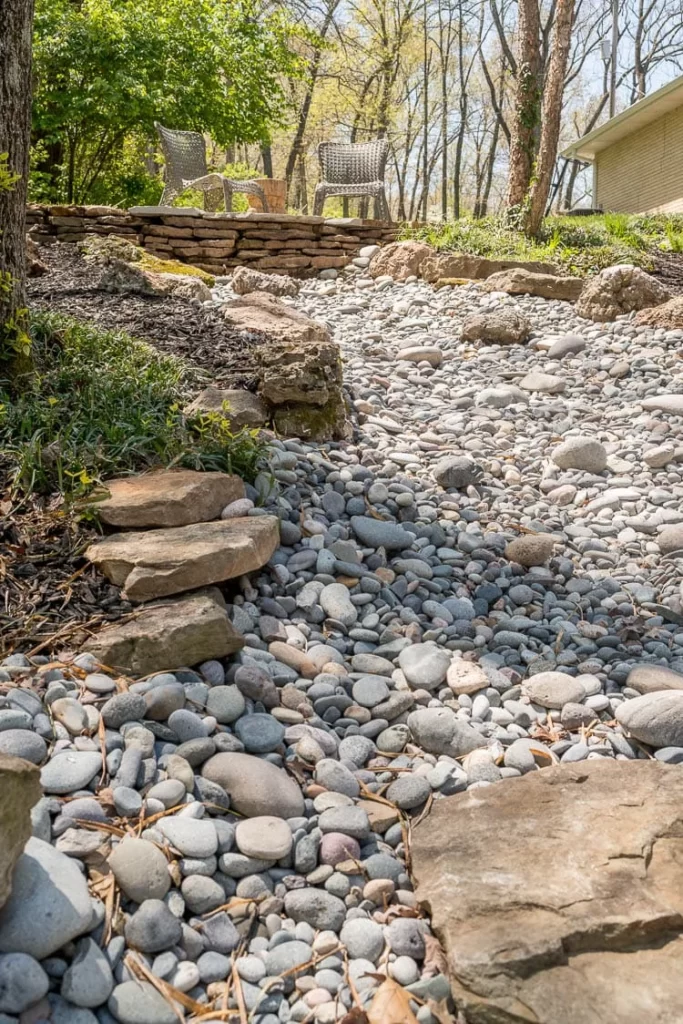 A river rock bed in a low pare of a yard with lots of rocks on each side of it.