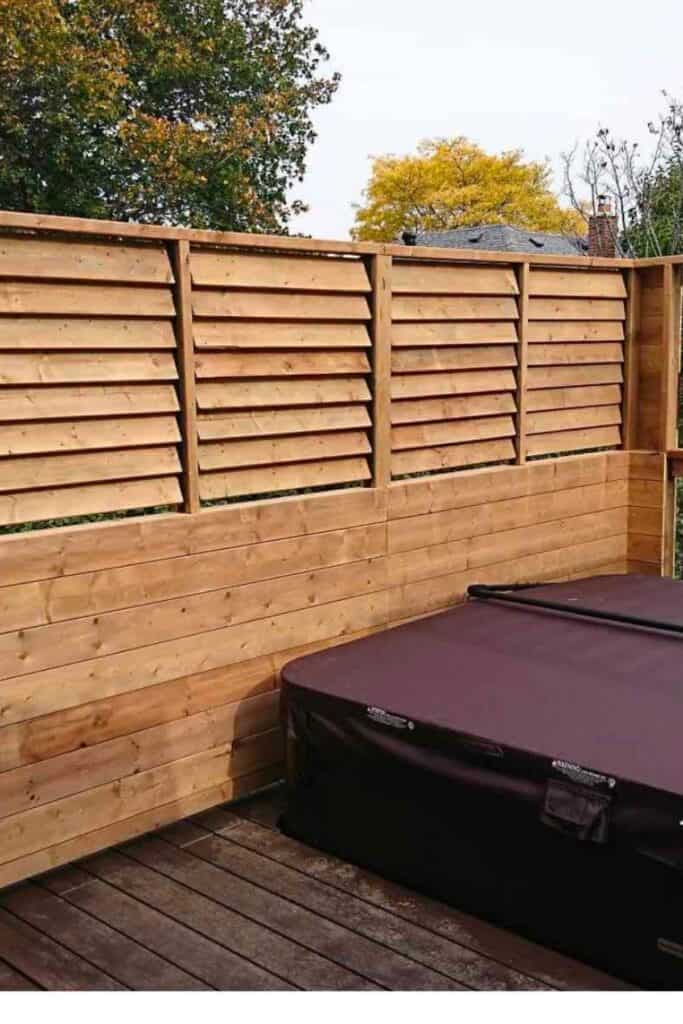 A horizontal privacy fence surrounding a hot tub that has a hard cover on it.
