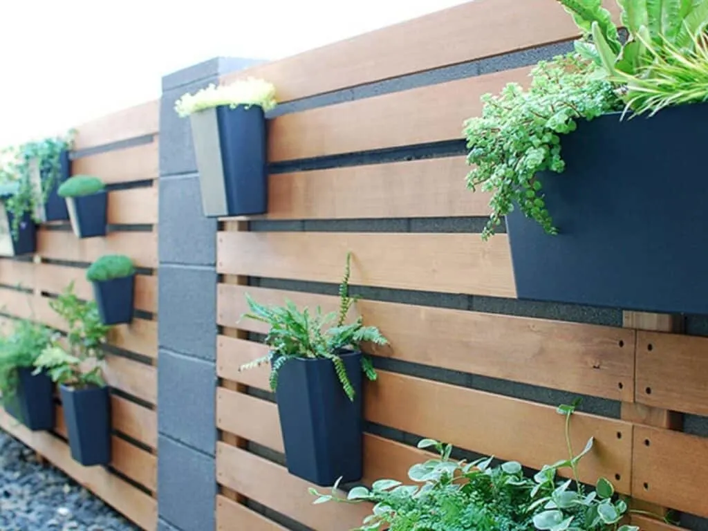 Horizontal wood fence with black flower pots and plants in them.