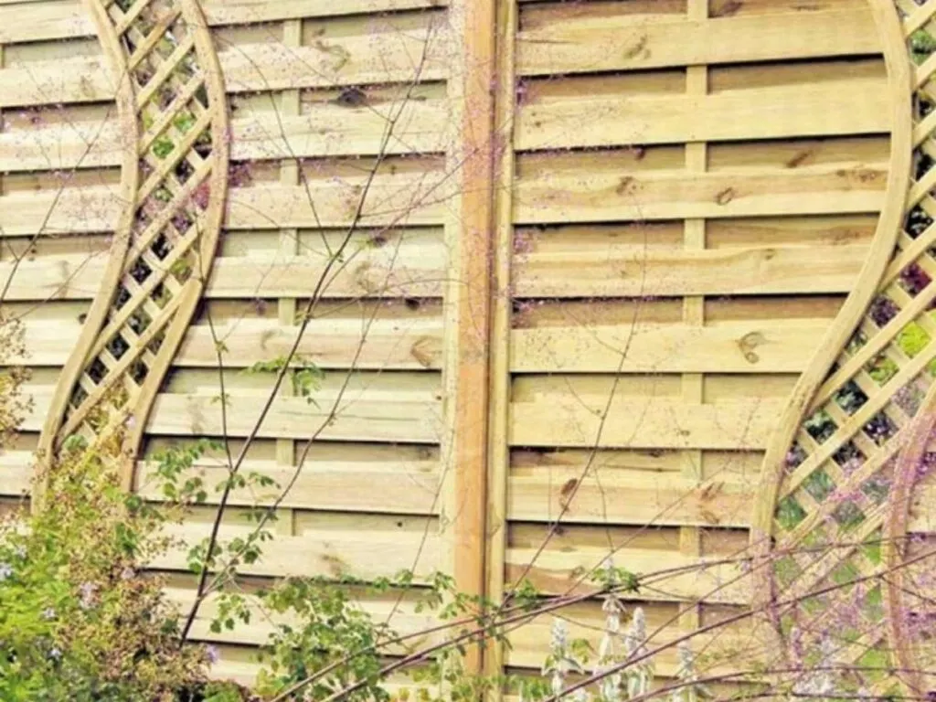 A wooden horizontal fence with curved cut outs of lattice work.
