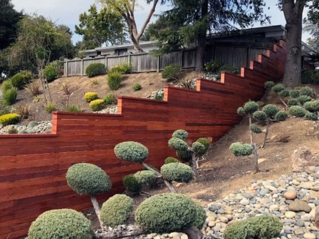 A modern horizontal fence stair stepping down a sloped yard with lots of plants and a rock garden.