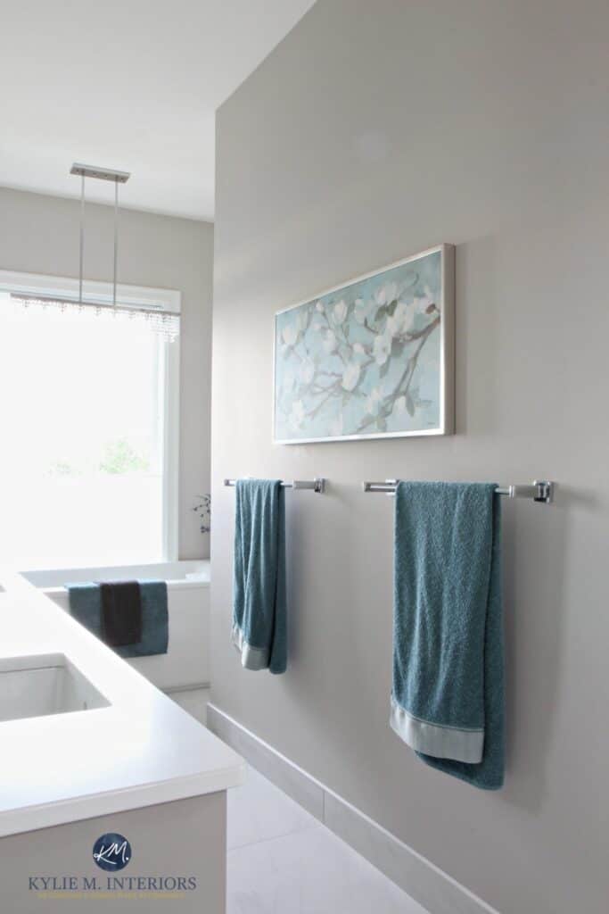 A bathroom with Balboa Mist on the walls, tons of light coming through a window and teal cover towels hanging from silver towel bars.