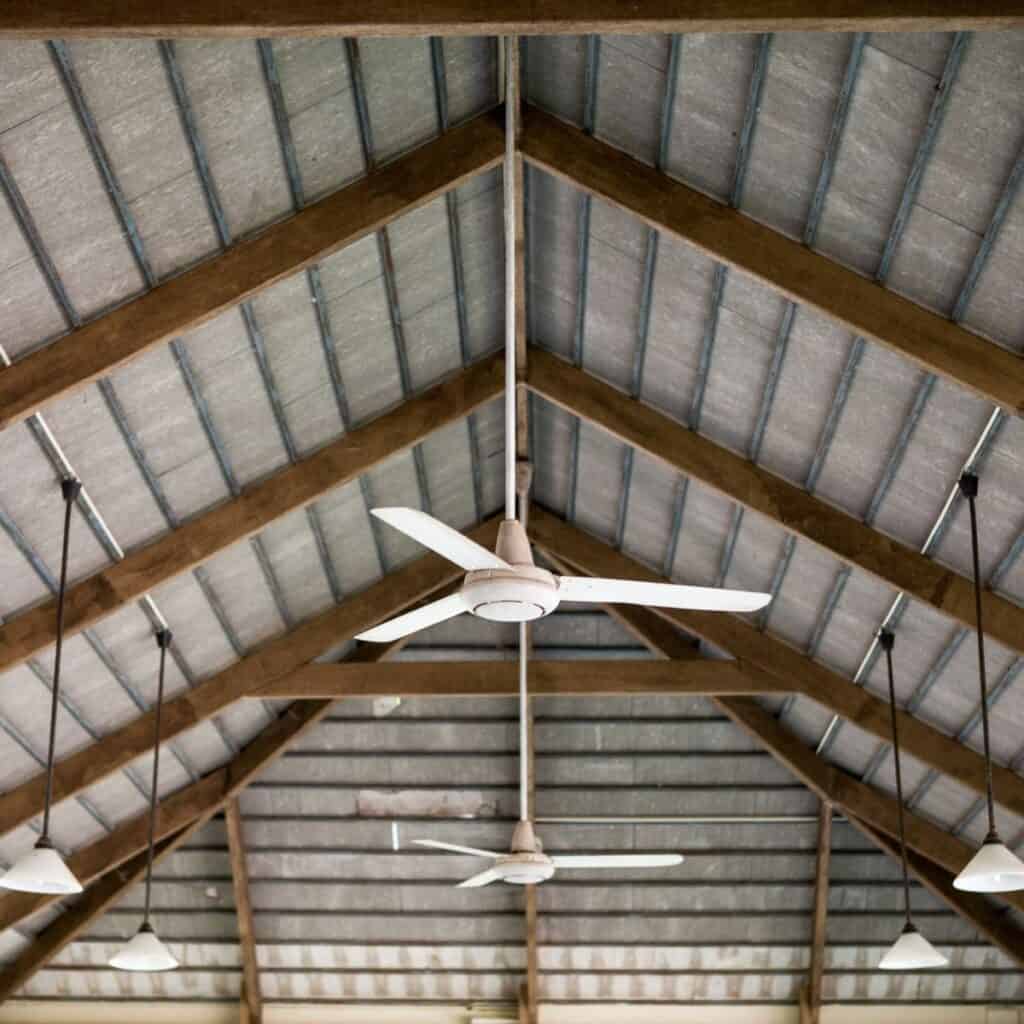 The ceiling of room with wood beams, metal roof and a white ceiling fan.