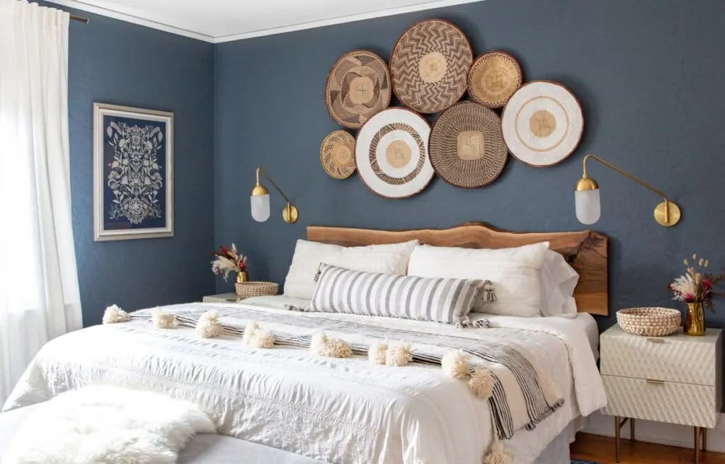A bedroom with white bedding and Hale Navy on the walls with a basket installation over the headboard.