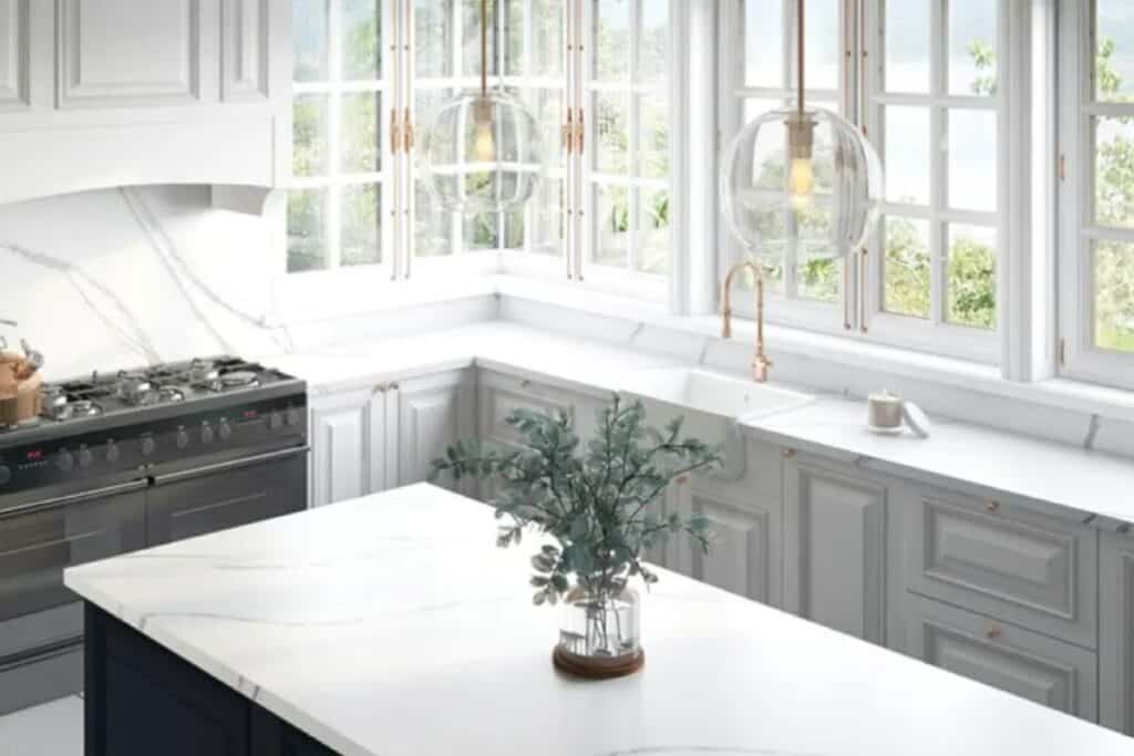Light gray cabinets, white marble looking counters with tons of windows and gold hardware.