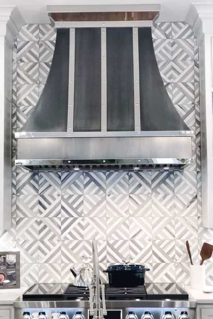 A gray and white backsplash with a stove vent hood of metal and gray.