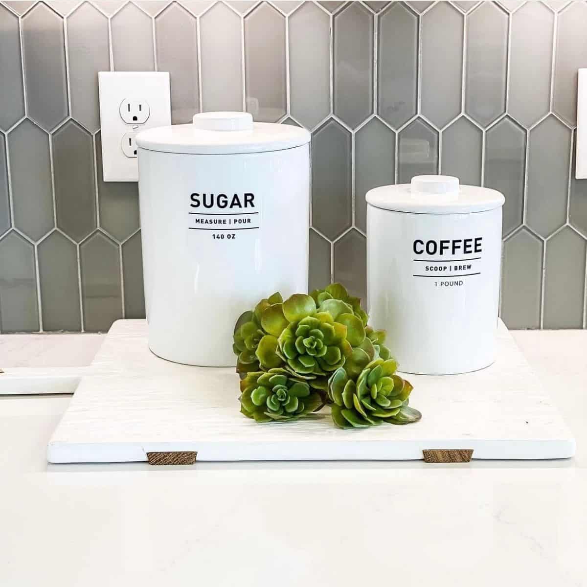 A vignette of a sugar and coffee canister sitting on a wood cutting board with succulents.