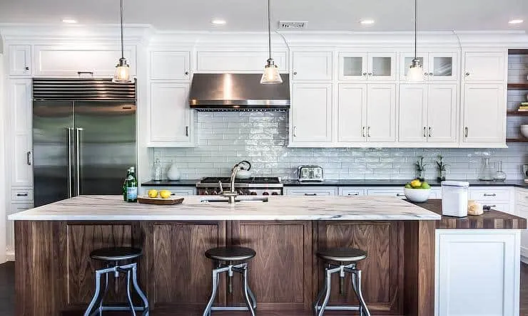 A white kitchen with subway tile backsplash, a dark wood island and stainless steel appliances.