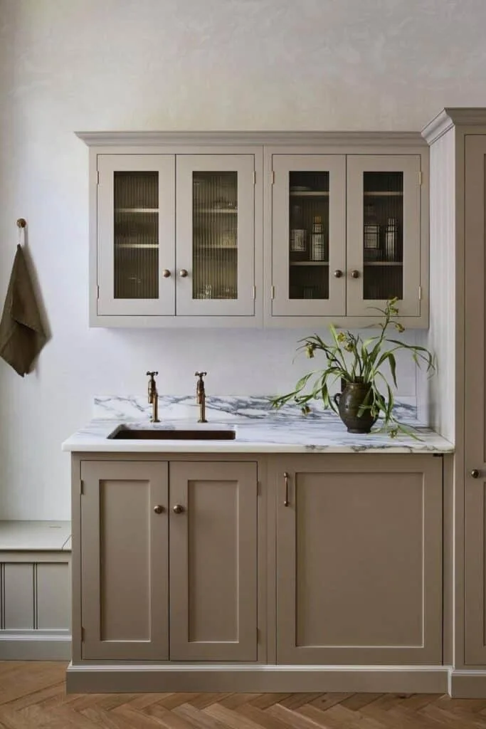 Taupe Cabinets with marble countertops, a plant and herringbone hardwood floors.