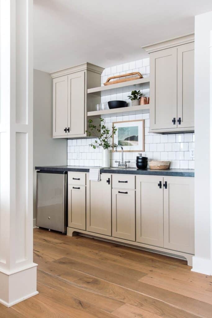 Greige kitchen cabinets with black hardware, black countertops and white subway tile backsplash.