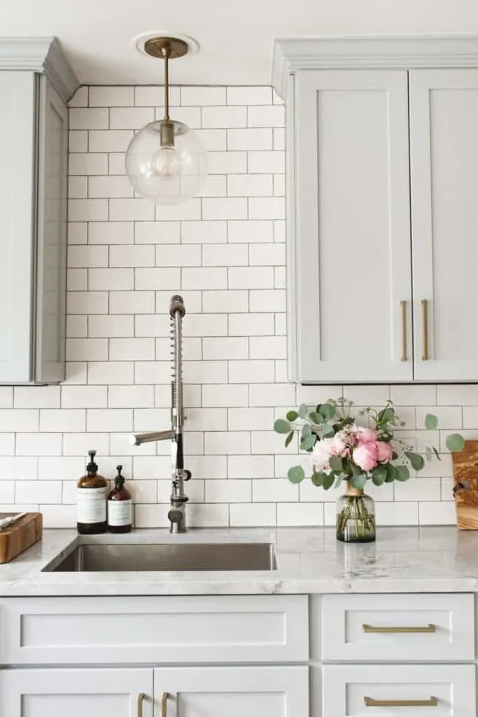light gray cabinets with white subway tile backsplash and pink peonies in a vase on the counter.