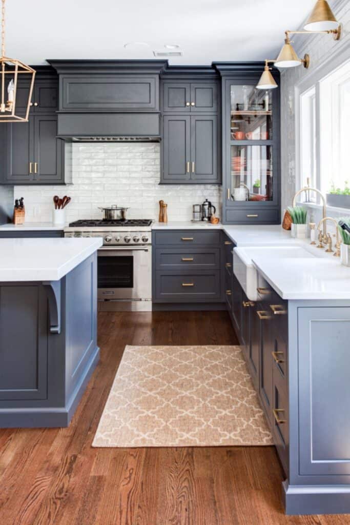 navy blue cabinets with gold hardware, gold light fixtures, white countertops, and a white subway tile backsplash.