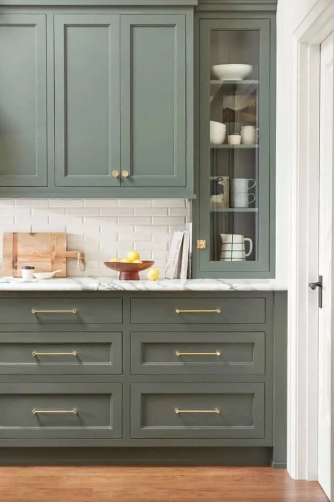 light green cabinets with a marble counter and white subway tile backsplash.