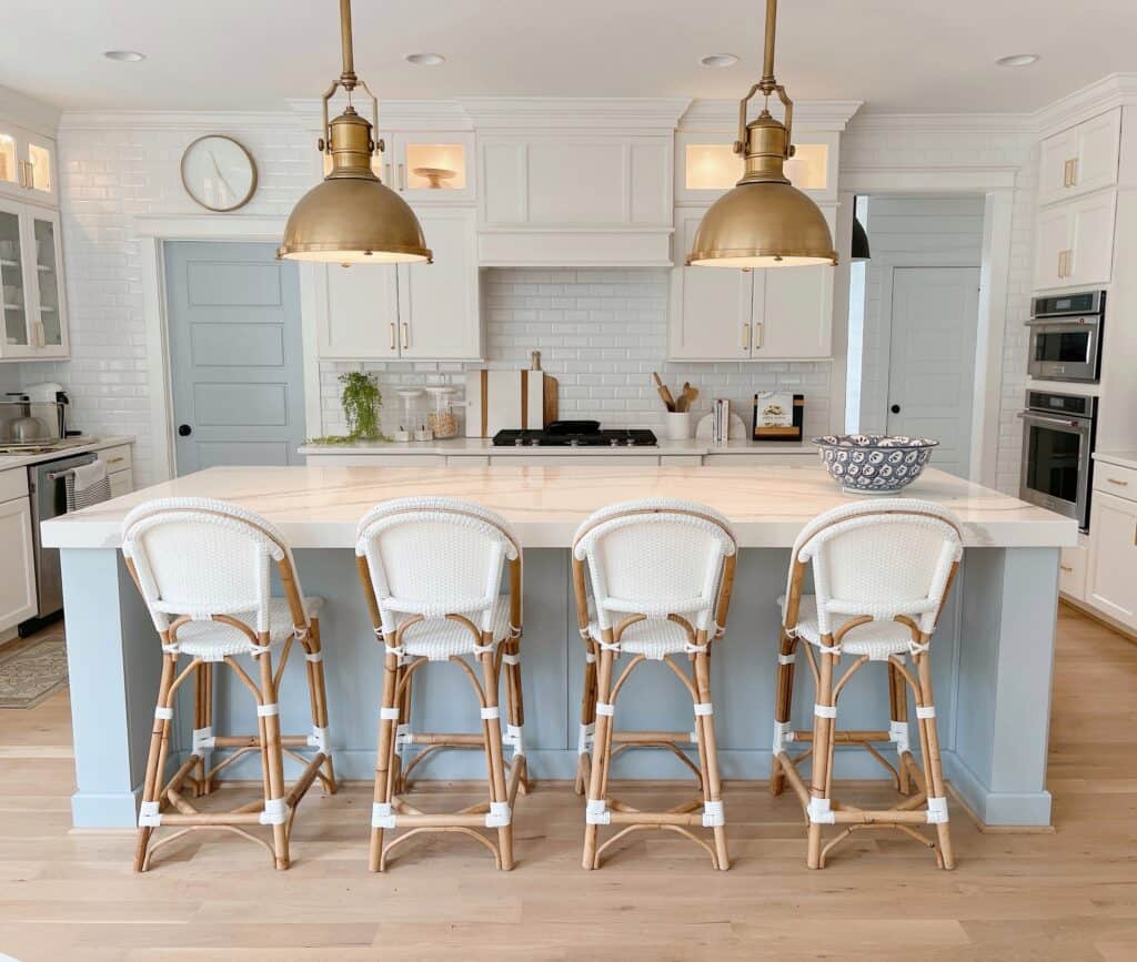 A light blue island with light hardwood floors, white counters and white/wood bar stools.