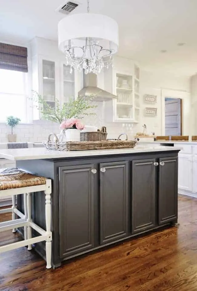A white kitchen with a very dark island, white counters, dark hardwood floors and crystal hardware on the island.