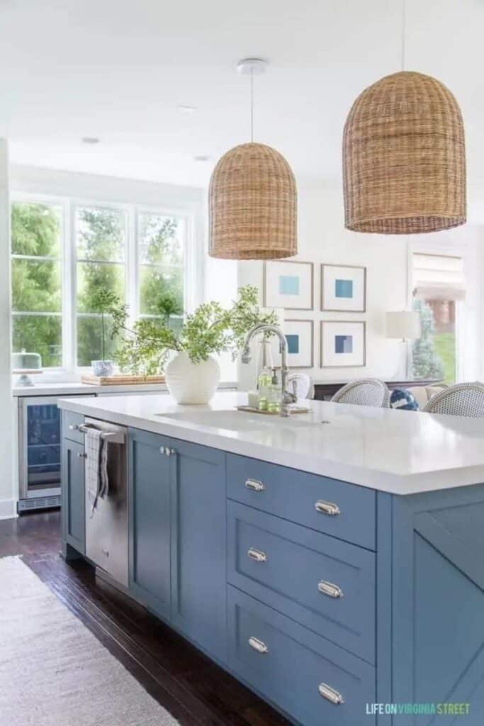 A medium to light blue island, silver hardware, dark wood floors and white countertops with stainless steel appliances.