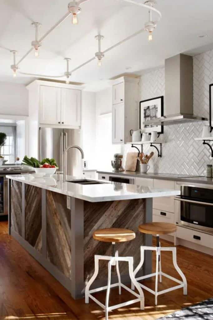 A white kitchen with a white subway tile backsplash in a herringbone pattern, black hardware, and a reclaimed wood island.