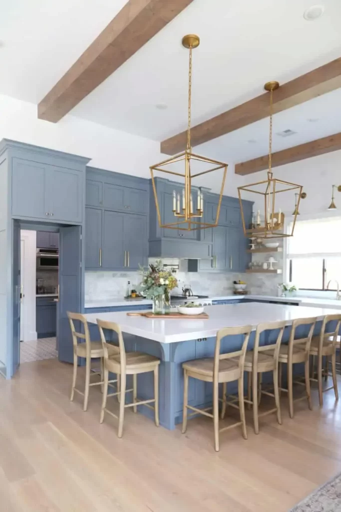 A light to medium blue kitchen with white countertops, gold hardware and light hardwood floors.