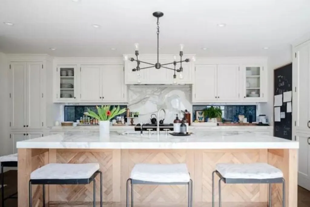A white kitchen with an island in light wood that has a herringbone pattern.