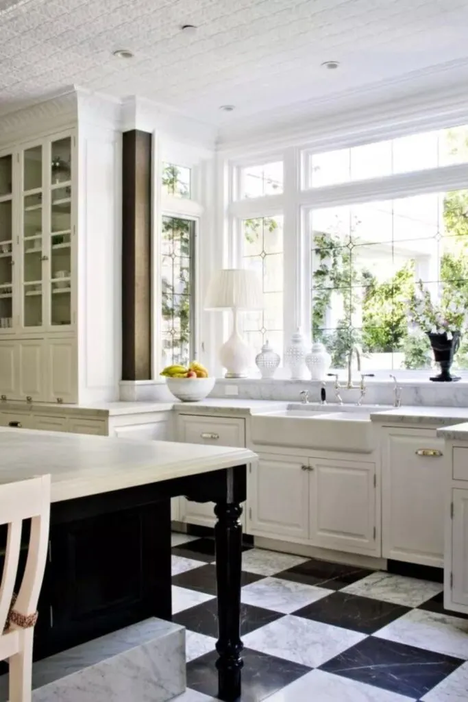 White perimeter cabinets and a black island on a black and white marble checkered floor.